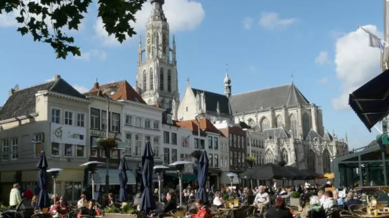 zicht op de Grote Markt van Breda: mensen op een terras en huizen en Onze Lievevrouwekerk op de achtergrond