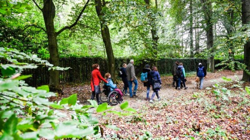 Groep mensen, waaronder iemand in rolstoel, loopt in het bos