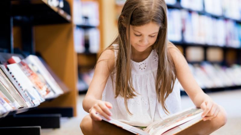 Meisje zit boek te lezen in bibliotheek