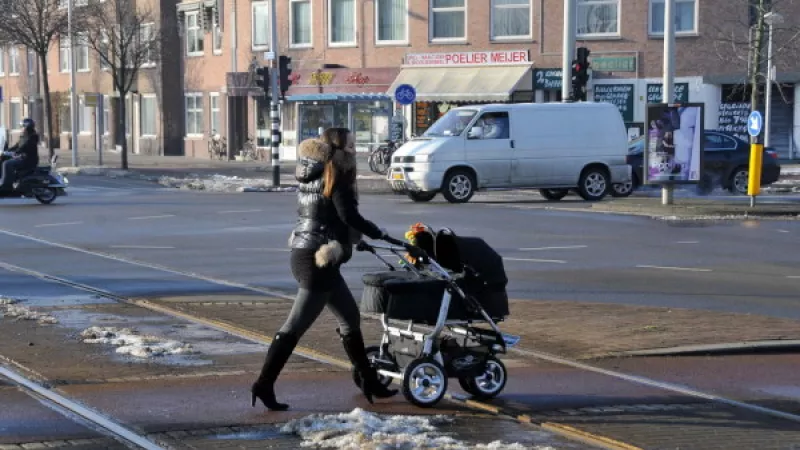 Moeder met kinderwagen steekt de straat over