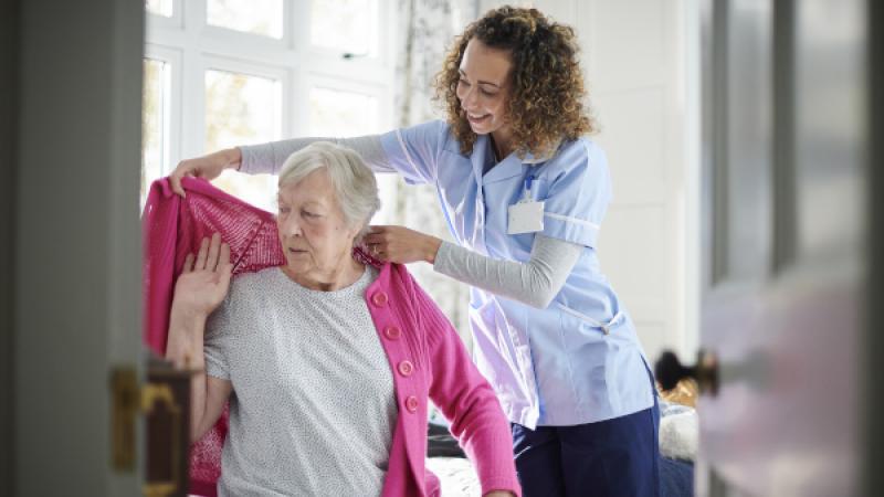 Oudere dame wordt geholpen met aankleden