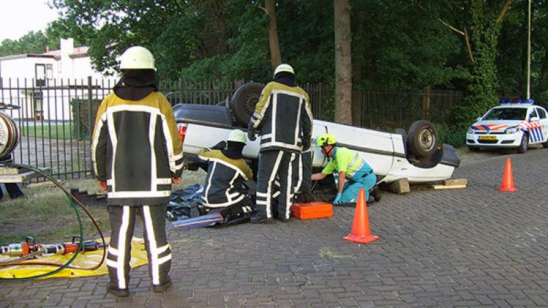 Brandweerlieden en ambulancepersoneel bij een over de kop geslagen auto