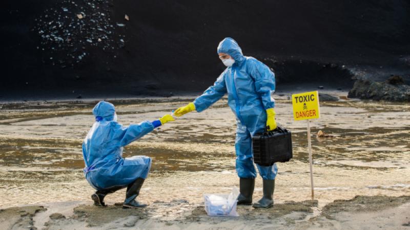 Twee mensen in beschermende pakken werken bij bordje Toxic & Danger