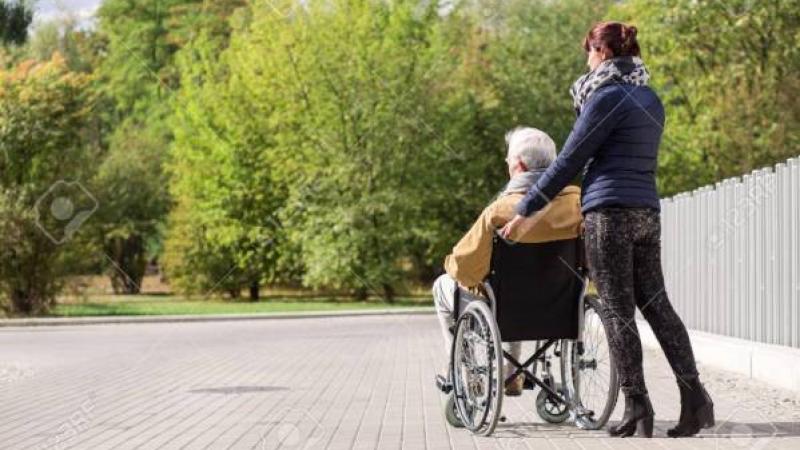 oudere man in rolstoel voortgeduwd door jongere vrouw
