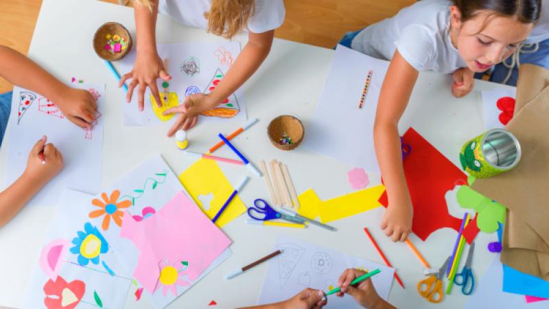 Bovenaanzicht van tafel met kleuters die aan het tekenen en plakken zijn