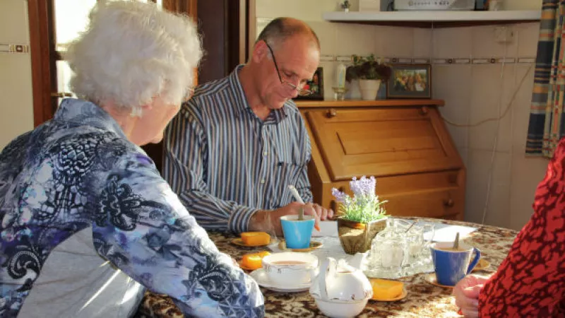 man aan eetkamertafel tekent formulier, vrouw kijkt toe