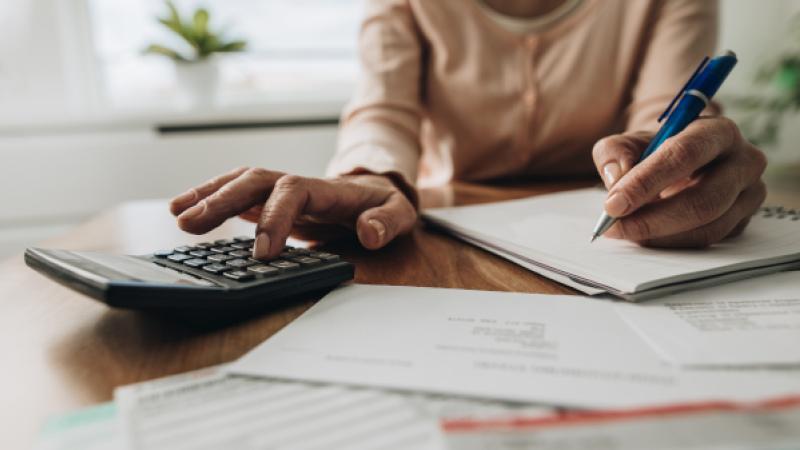 vrouw achter bureau met rekeningen en rekenapparaat