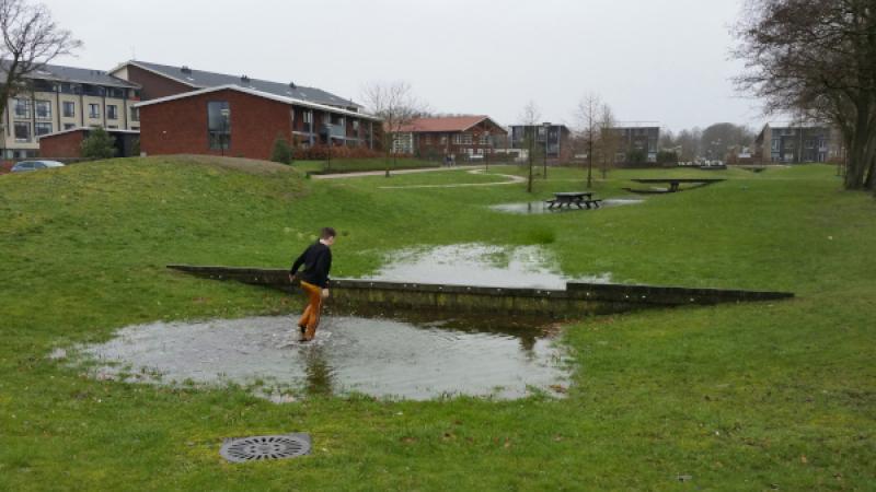Kind speelt in plas water op groen veldje bij huizen