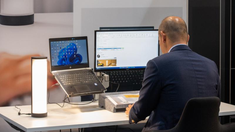 man (op de rug gezien) aan bureau achter computer/beeldscherm en laptop