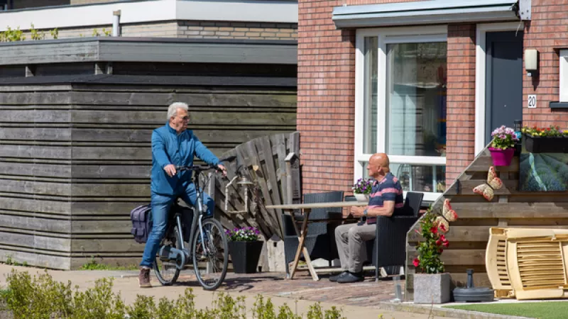 Een man op een fiets praat met een man die in de voortuin zit