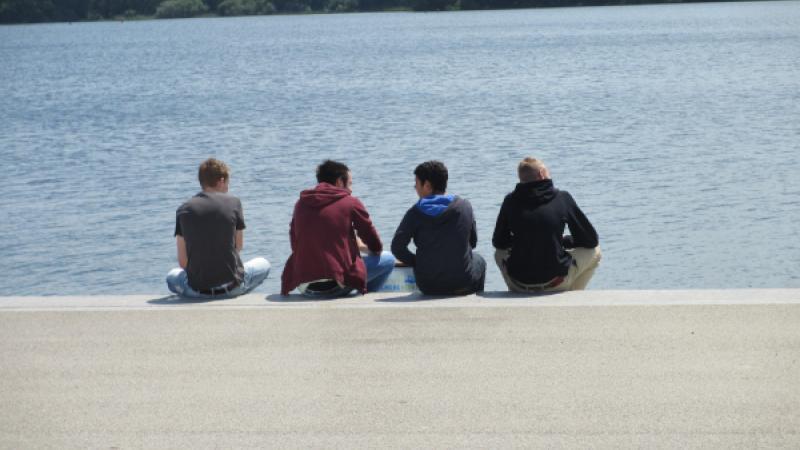 Jongeren zitten langs het water met rug naar camera