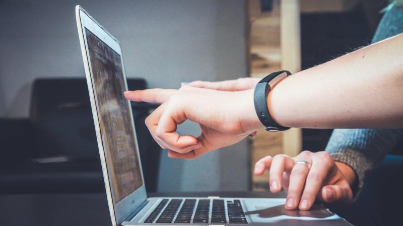 twee mensen wijzen een computerscherm aan, ze bekijken samen iets op het scherm