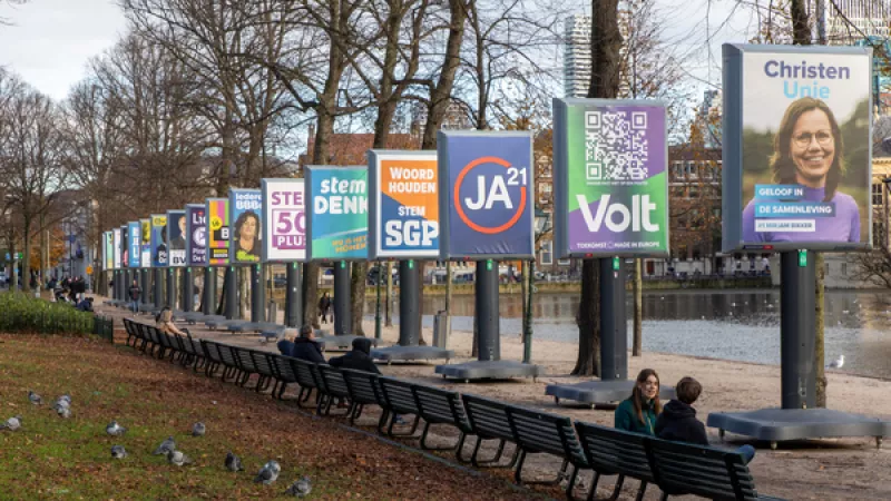 rij verkiezingsborden naast de Hofvijver in Den Haag, daarnaast bankjes op een rij met mensen