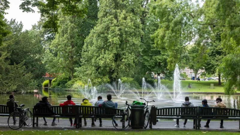 Mensen zitten op bankjes in een park, voor een fontein