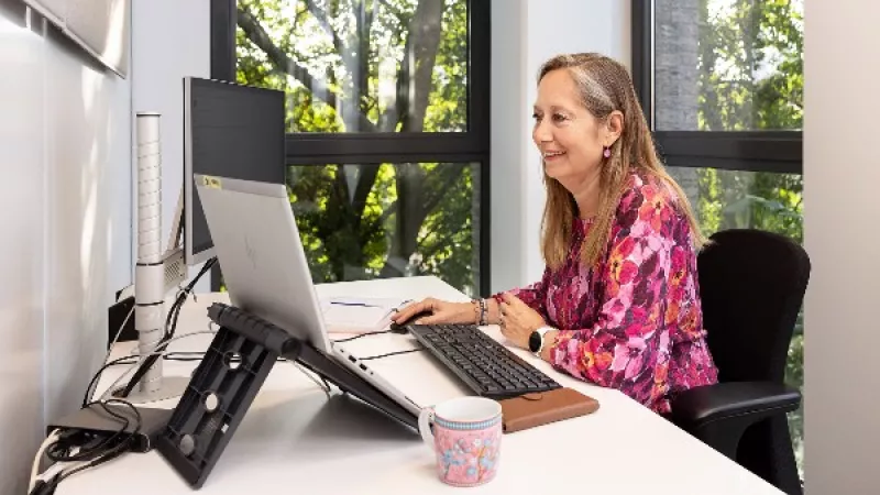 Vrouw aan het werk aan een bureau met laptop, toetsenbord en beeldscherm