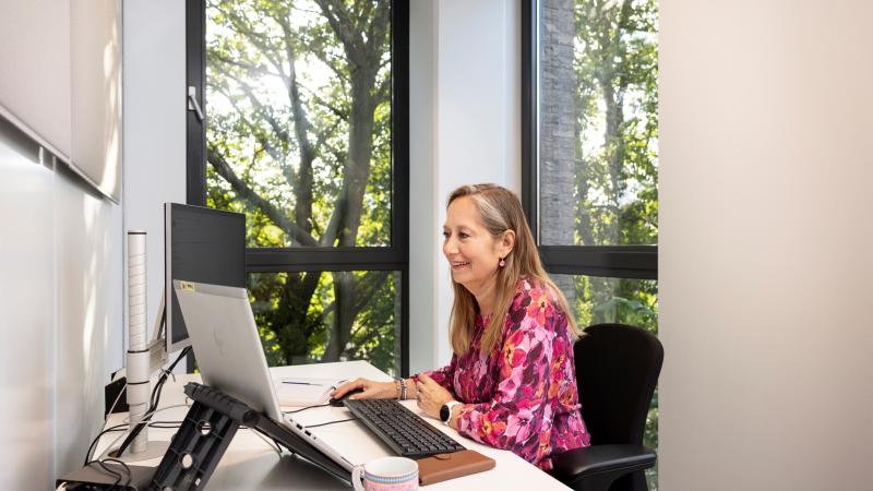 Vrouw aan het werk aan een bureau met laptop, toetsenbord en beeldscherm