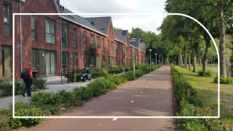 Iemand loopt langs een rij huizen met een fietspad en bomen ervoor