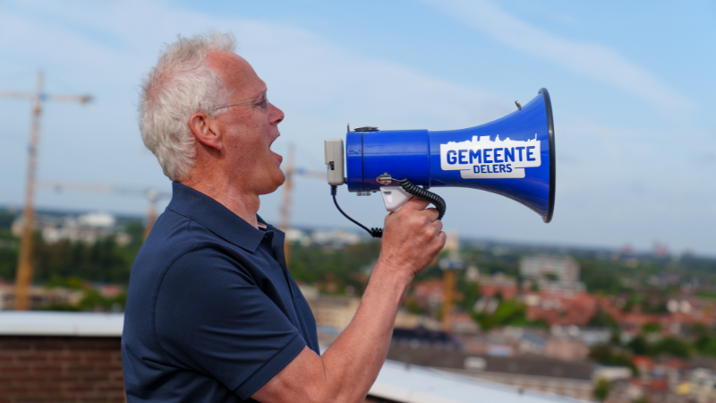 Een man roept met een GemeenteDelers megafoon in zijn hand.