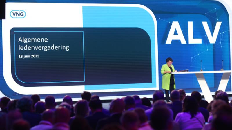 Sharon Dijksma op het podium achter een tafel, achter haar de teksten 'ALV' en 'Algemene ledenvergadering 18 juni 2025' met het VNG-logo
