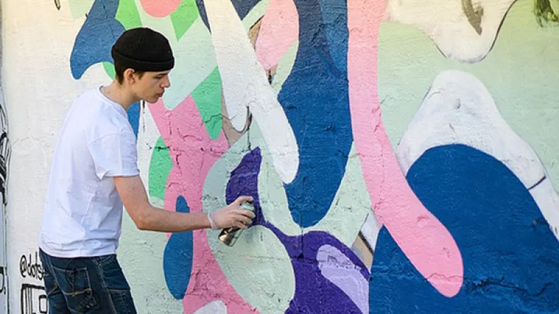 Een jongen maakt een tekening van graffiti op een muur