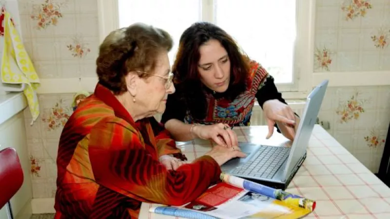 Oudere en jongere vrouw aan keukentafel achter een laptop