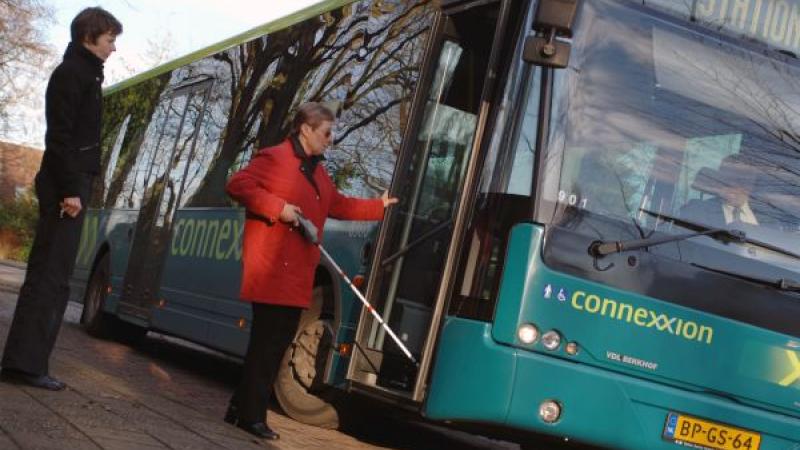 Vrouw met blindengeleidestok stapt in bus