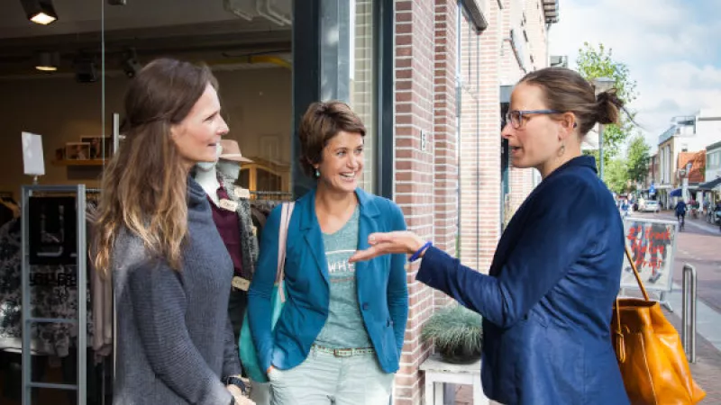 Drie vrouwen met elkaar in gesprek bij de ingang van een winkel
