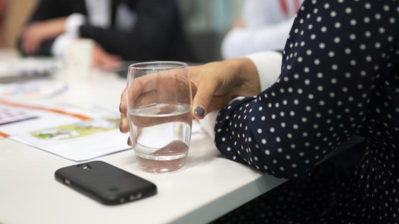 Close-up van hand met glas water op vergadertafel