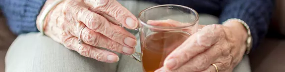 Handen van een bejaarde dame die een kop thee vast houdt