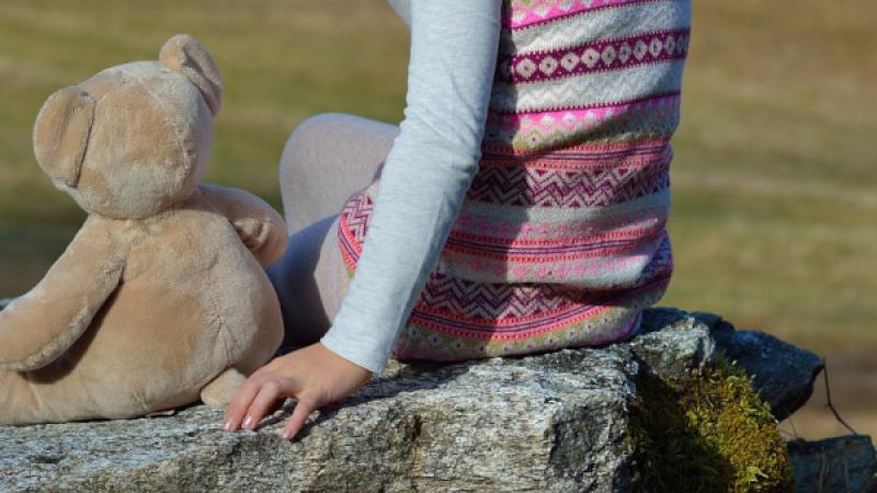 kind zit buiten op een steen met een knuffelbeer