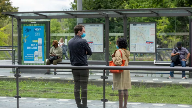 Mensen met mondkapjes staan te wachten bij een tramhalte