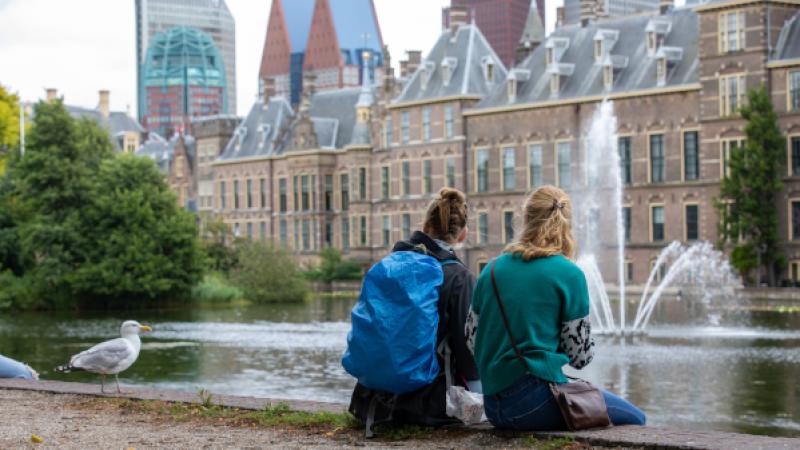 Twee vrouwen en een meeuw zitten aan de hofvijver tegenover Binnenhof