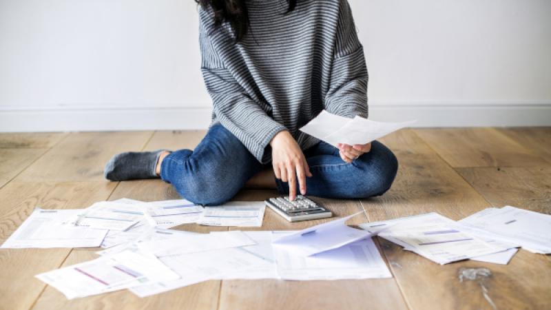 Vrouw zit op de grond met rekenmachine, omringd door rekeningen