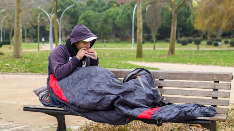 Dakloze man met slaapzak op bankje in park