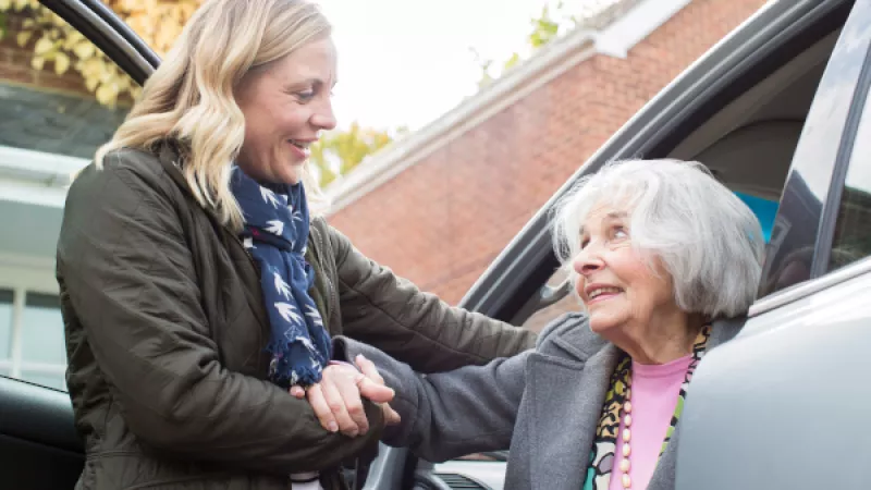 Oudere dame wordt uit auto geholpen