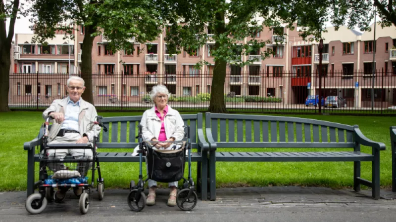 oudere man en vrouw (met rollators) op bank in park