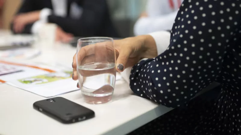 Vrouwenhand met glas water aan vergadertafel