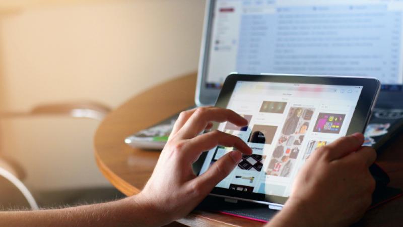 Iemand werkt op zijn tablet, op de achtergrond zie je een laptop staan