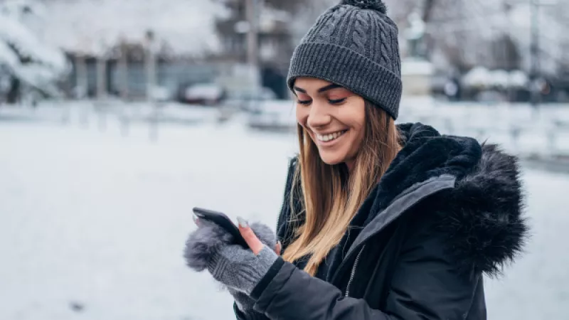 Tienermeisje staat buiten in de sneeuw en lacht naar mobiele telefoon in haar hand