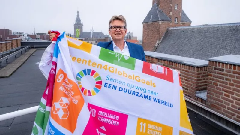 Een man staat op het dak en toont de Global Goals-vlag