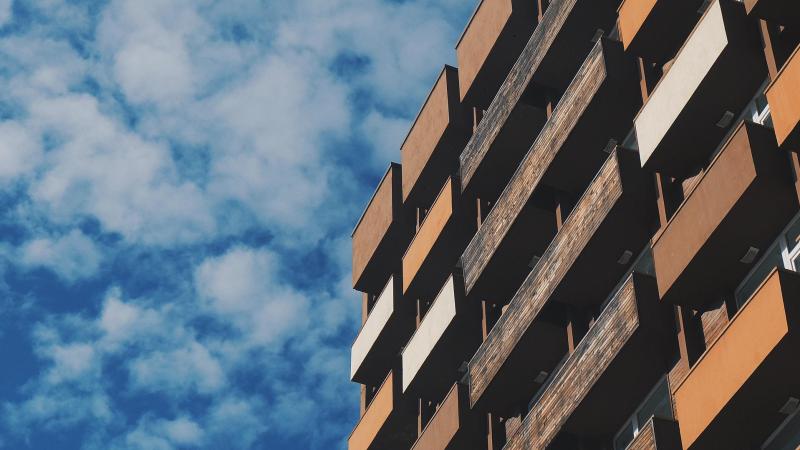 Flatgebouw met meerdere balkons en daarachter een blauwe lucht