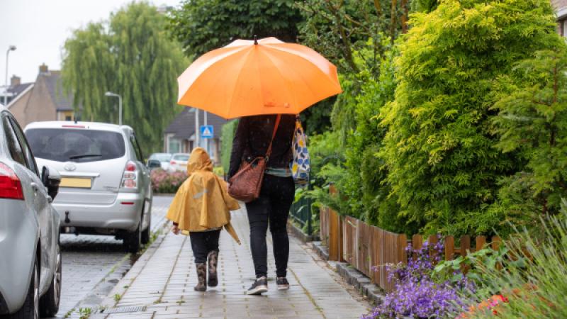 Ouder en kind lopen in regen onder paraplu