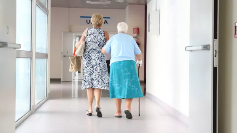 Twee vrouwen lopen arm aan arm in de hal van een ziekenhuis