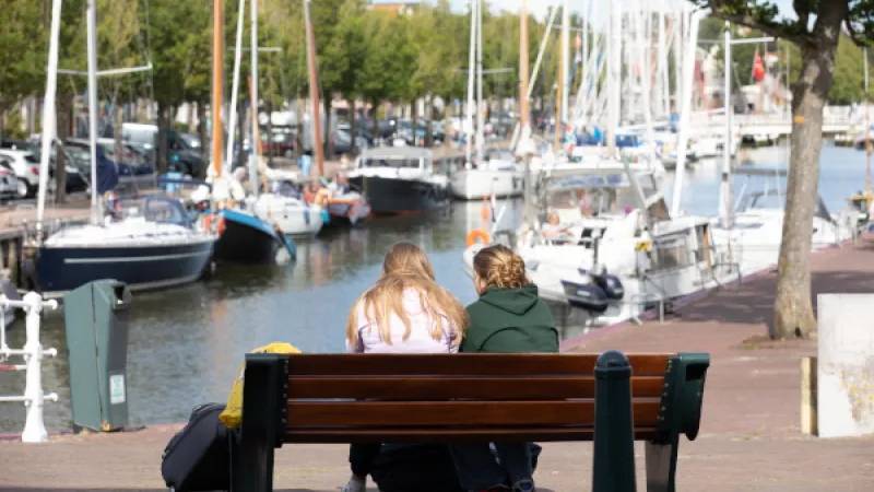 2 tienermeisjes zitten op bankje bij haven