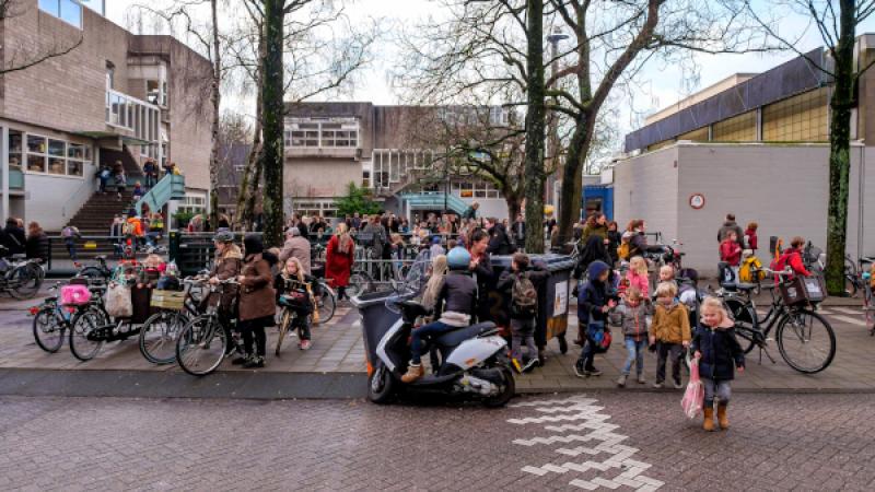 Veel mensen en kinderen staan voor een schoolgebouw