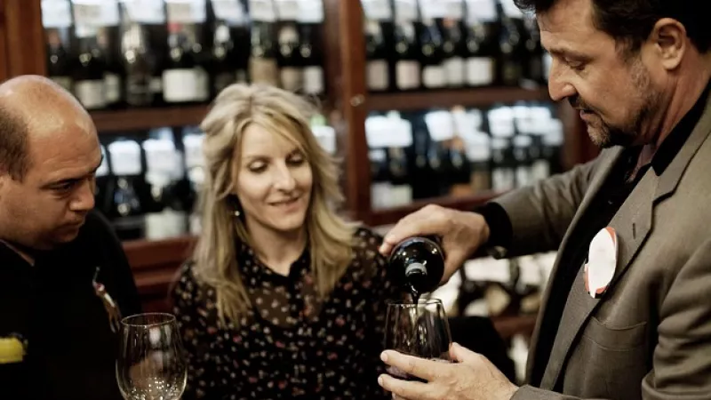 winkelier wijnbar schenkt glas wijn in voor klanten (man en vrouw)