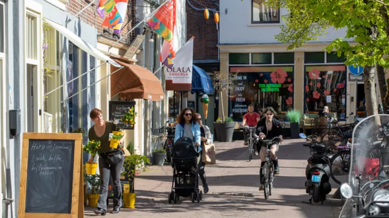 winkelstraat met fietsers en vrouw met kinderwagen, vlaggen aan de gevels