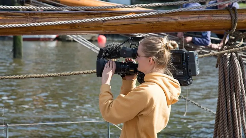 cameravrouw met camera op schouder bij waterevenement