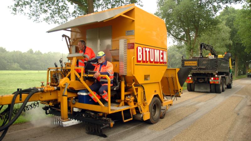 Twee mannen werken met een grote machine aan de weg
