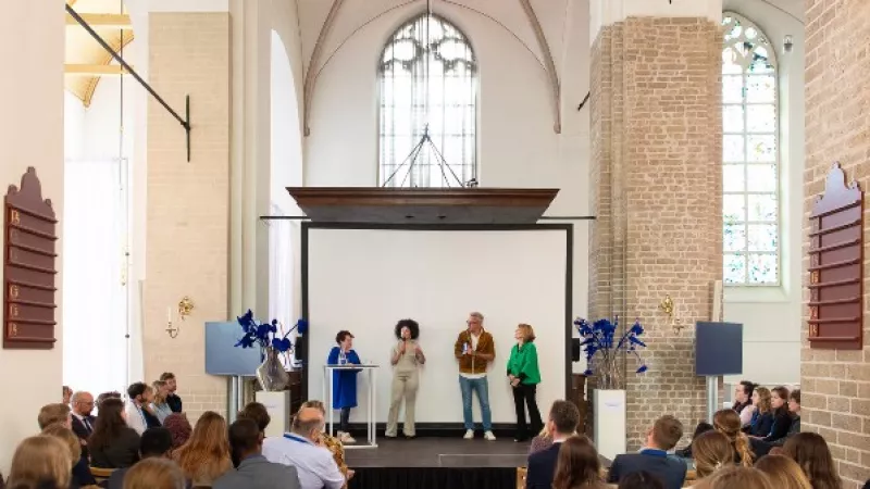 Een jongere aan het woord op het podium in een kerk, met naast haar Sharon Dijksma
